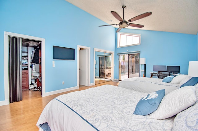 bedroom featuring multiple closets, light hardwood / wood-style floors, ceiling fan, high vaulted ceiling, and a textured ceiling