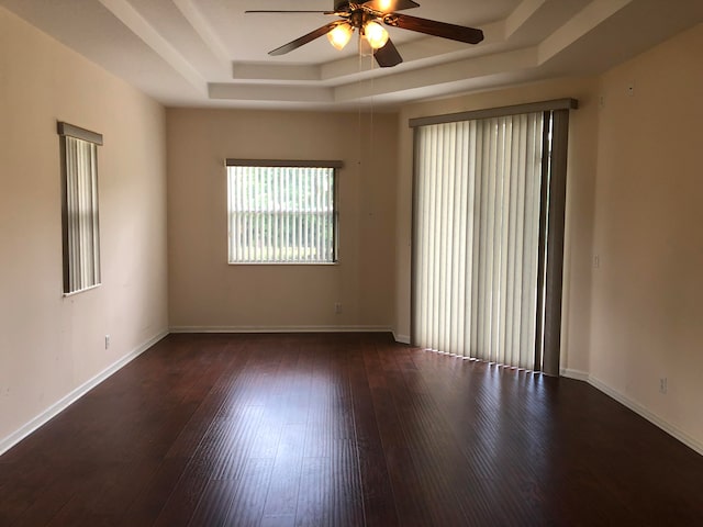 empty room with dark hardwood / wood-style flooring, ceiling fan, and a raised ceiling