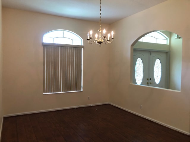 unfurnished room featuring a wealth of natural light, dark wood-type flooring, and an inviting chandelier