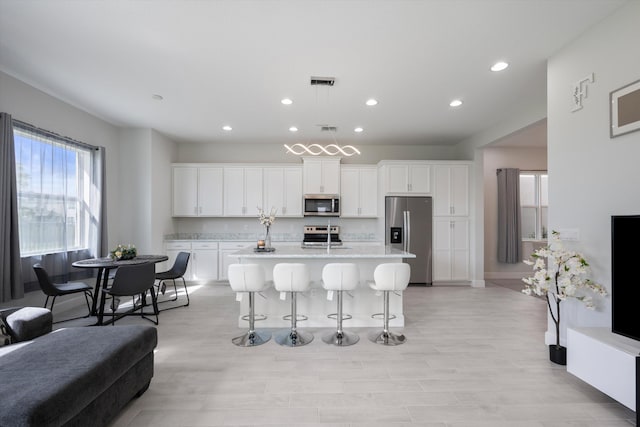 kitchen with white cabinets, a kitchen breakfast bar, stainless steel appliances, a center island with sink, and decorative light fixtures