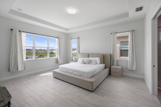 bedroom with light wood-type flooring and a raised ceiling