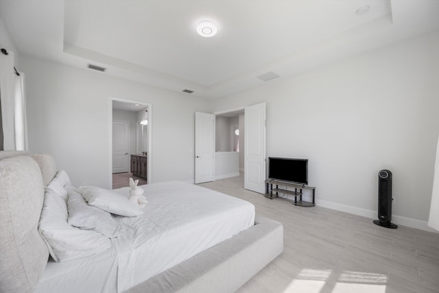 bedroom featuring light hardwood / wood-style flooring, a raised ceiling, and ensuite bathroom