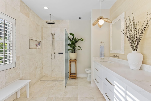 bathroom with toilet, a tile shower, and vanity