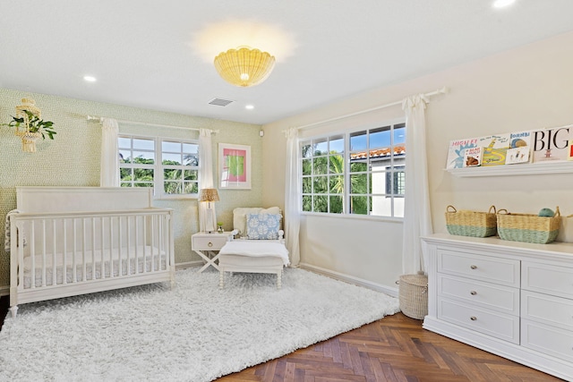 bedroom featuring multiple windows, a crib, and parquet flooring