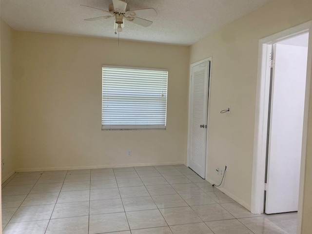 spare room featuring ceiling fan, light tile patterned flooring, and a textured ceiling