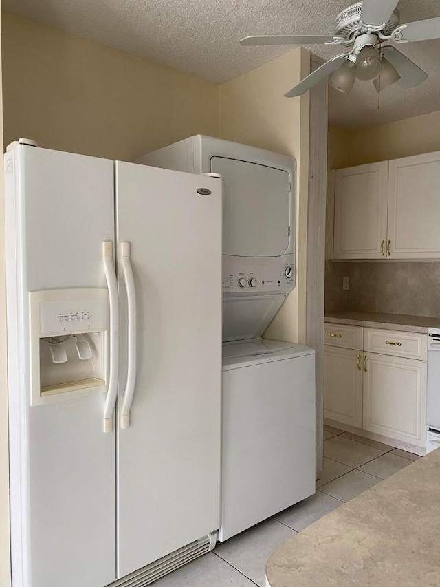 laundry room featuring a textured ceiling, stacked washer and clothes dryer, ceiling fan, and light tile patterned floors