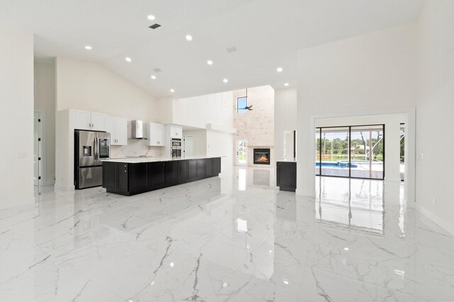 kitchen featuring a high ceiling, appliances with stainless steel finishes, a fireplace, and wall chimney range hood