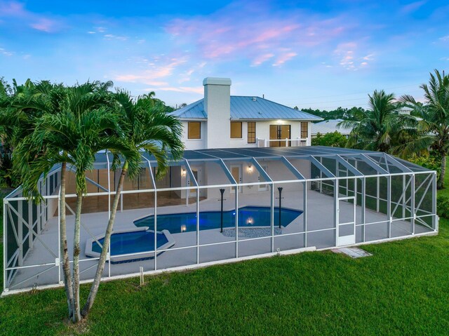 pool at dusk with glass enclosure, a lawn, and a patio