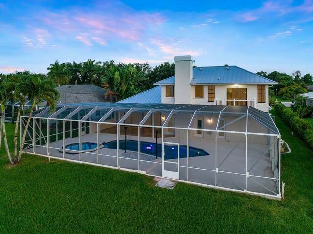 back house at dusk featuring a lawn, a patio, and glass enclosure