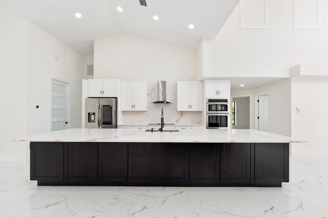 kitchen with stainless steel appliances, high vaulted ceiling, a large island, wall chimney range hood, and white cabinets