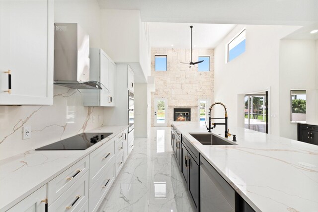 kitchen with a high ceiling, decorative light fixtures, sink, appliances with stainless steel finishes, and wall chimney range hood