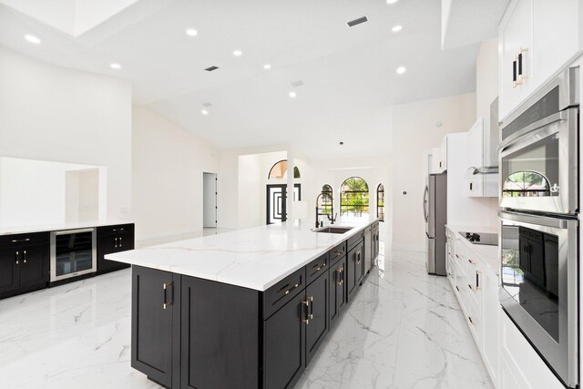 kitchen featuring beverage cooler, stainless steel appliances, sink, a large island with sink, and light stone counters