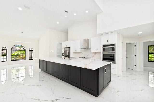 kitchen with wall chimney range hood, a healthy amount of sunlight, white cabinets, and a large island