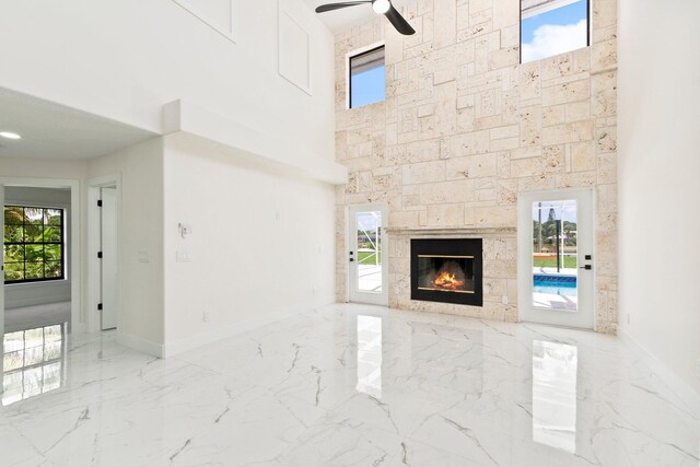 unfurnished living room featuring a healthy amount of sunlight, ceiling fan, and a stone fireplace