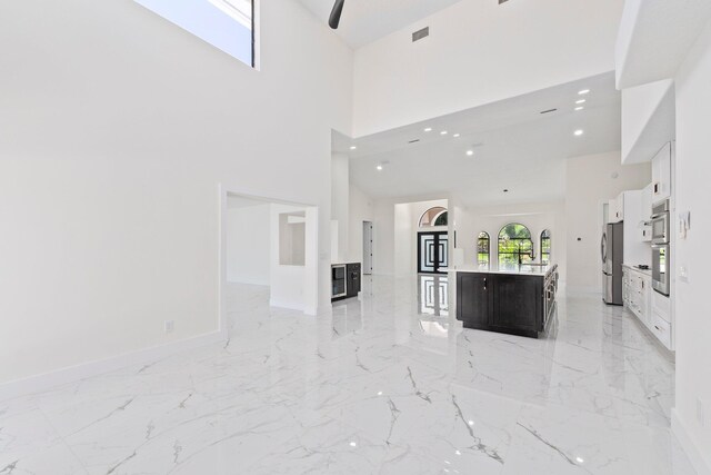 kitchen with a towering ceiling, stainless steel fridge, white cabinetry, and an island with sink