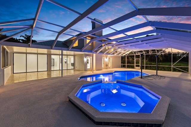 pool at dusk featuring a patio area, glass enclosure, and an in ground hot tub