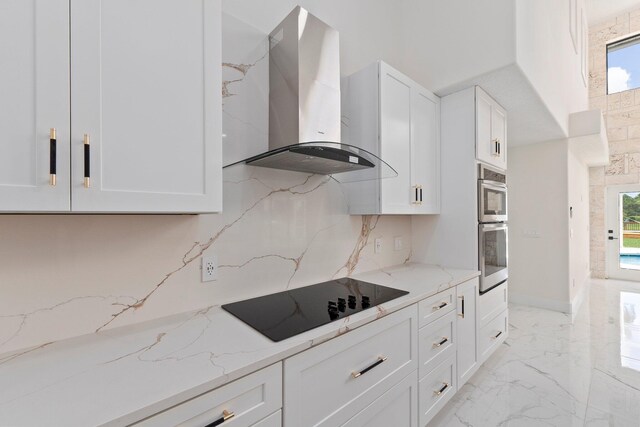 kitchen featuring light stone countertops, white cabinetry, black electric cooktop, wall chimney range hood, and double oven