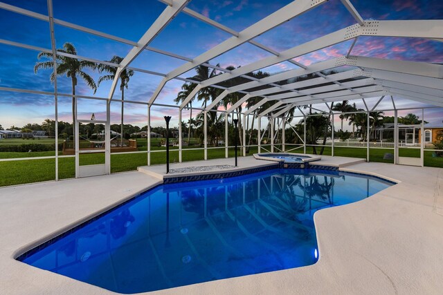 pool at dusk with glass enclosure, a patio, a lawn, and an in ground hot tub