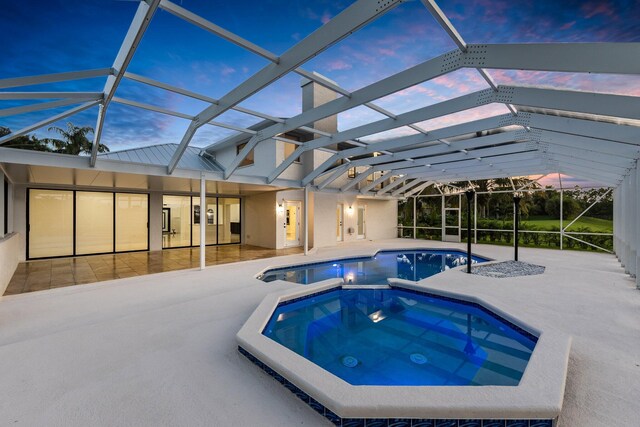 pool at dusk featuring a patio area, glass enclosure, and an in ground hot tub