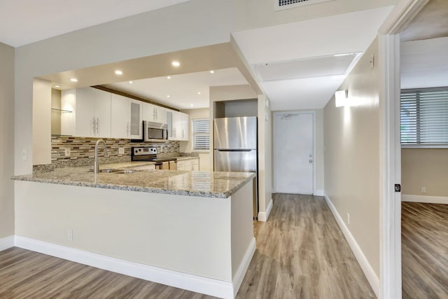 kitchen with light wood-type flooring, white cabinets, stainless steel appliances, and kitchen peninsula