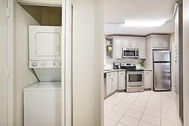 kitchen with appliances with stainless steel finishes, stacked washing maching and dryer, sink, light tile patterned flooring, and a textured ceiling