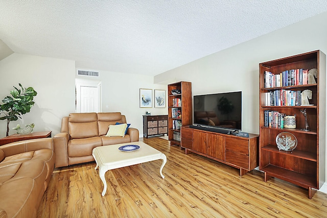 living room featuring lofted ceiling, light hardwood / wood-style floors, and a textured ceiling