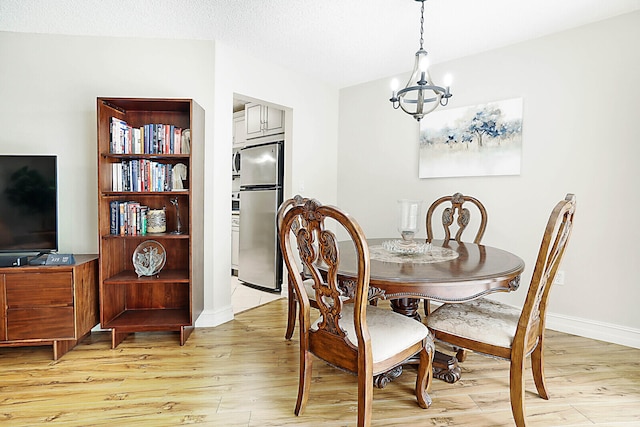 dining space with a textured ceiling, a notable chandelier, and light wood-type flooring