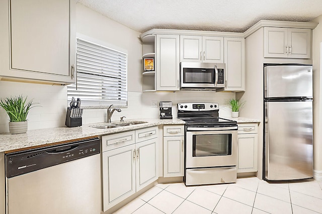 kitchen with a textured ceiling, light tile patterned floors, stainless steel appliances, sink, and light stone countertops