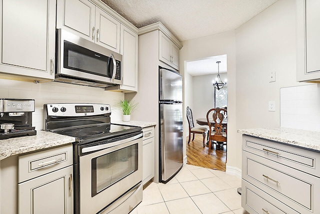 kitchen featuring a notable chandelier, a textured ceiling, stainless steel appliances, light stone counters, and light hardwood / wood-style floors