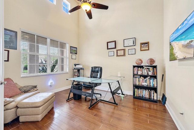 office featuring hardwood / wood-style floors, ceiling fan, and a towering ceiling