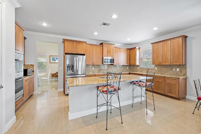 kitchen with an island with sink, a kitchen bar, light tile patterned flooring, and stainless steel appliances