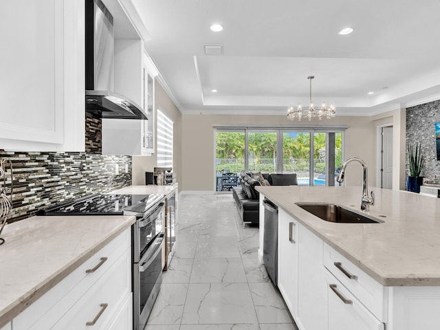 kitchen with sink, wall chimney exhaust hood, hanging light fixtures, light stone counters, and appliances with stainless steel finishes