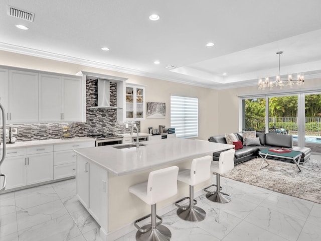 kitchen featuring sink, wall chimney range hood, a kitchen breakfast bar, pendant lighting, and a kitchen island with sink