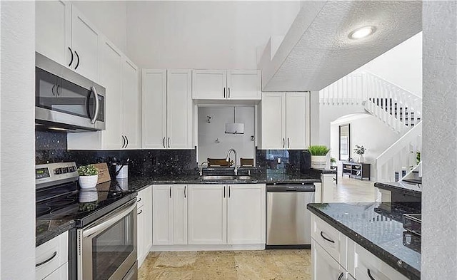 kitchen with stainless steel appliances, dark stone counters, white cabinetry, and sink