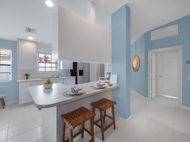 kitchen with white cabinetry, kitchen peninsula, light tile patterned floors, a kitchen bar, and stainless steel refrigerator with ice dispenser