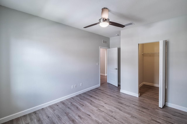 unfurnished bedroom featuring a walk in closet, ceiling fan, hardwood / wood-style flooring, and a closet