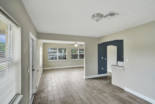 empty room featuring a wealth of natural light, ceiling fan, a textured ceiling, and light wood-type flooring