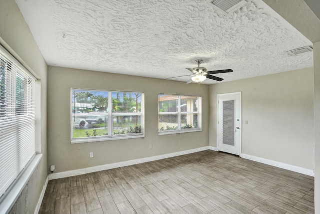 empty room with a textured ceiling, light hardwood / wood-style floors, a wealth of natural light, and ceiling fan