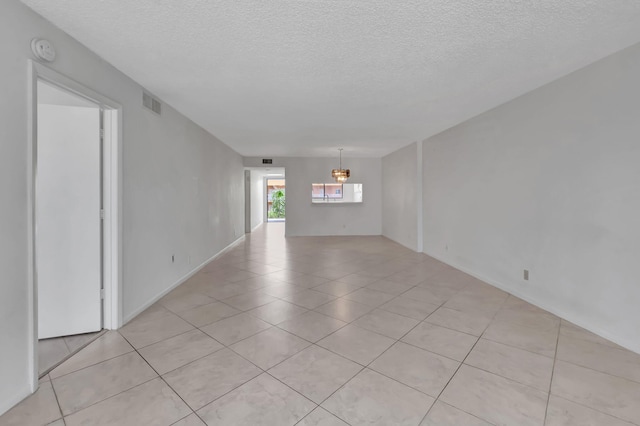 tiled empty room with a textured ceiling and an inviting chandelier