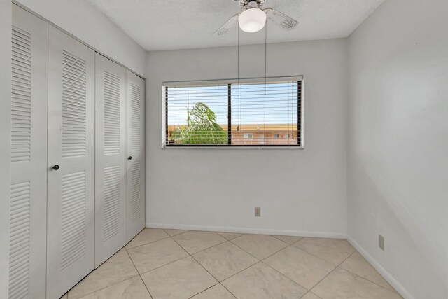 unfurnished bedroom with a textured ceiling, a closet, ceiling fan, and light tile patterned floors