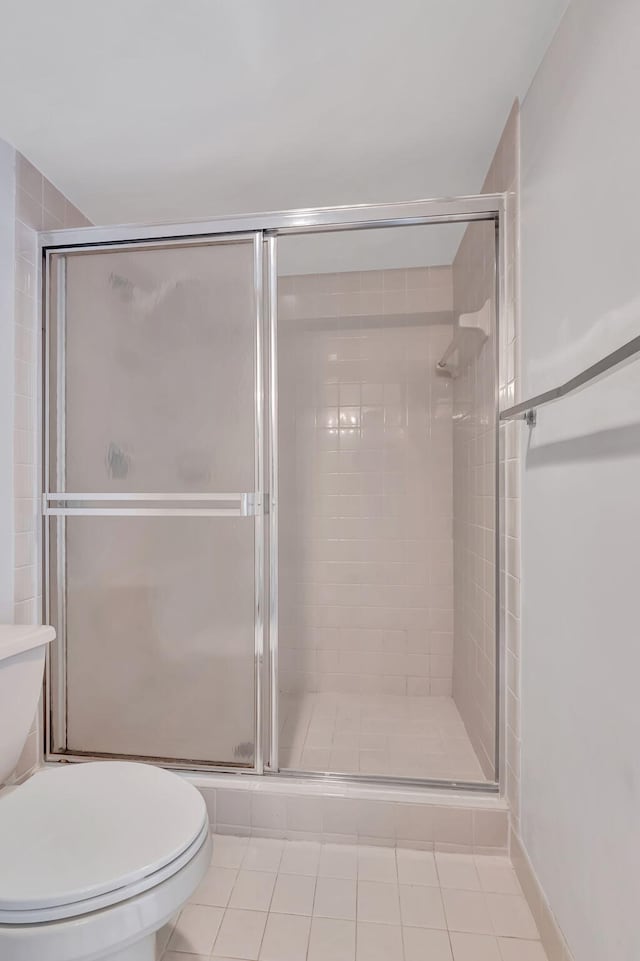 bathroom with a shower with door, toilet, and tile patterned floors