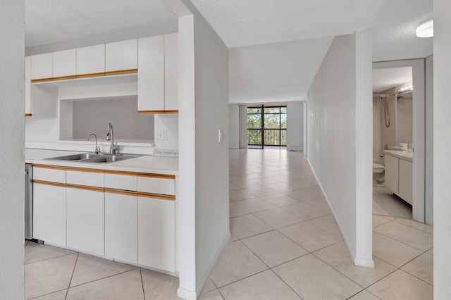 kitchen with white cabinetry, sink, light tile patterned flooring, and a textured ceiling