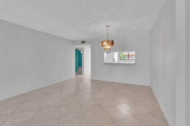 tiled empty room featuring a textured ceiling and a chandelier