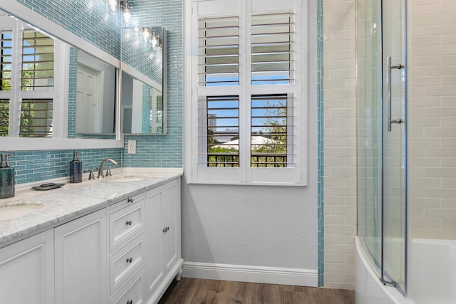 bathroom with hardwood / wood-style floors, vanity, tasteful backsplash, and bath / shower combo with glass door