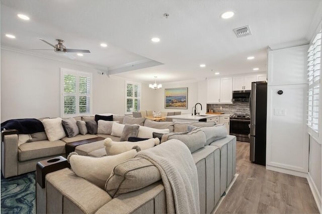 living room featuring ceiling fan with notable chandelier, light hardwood / wood-style flooring, ornamental molding, and sink