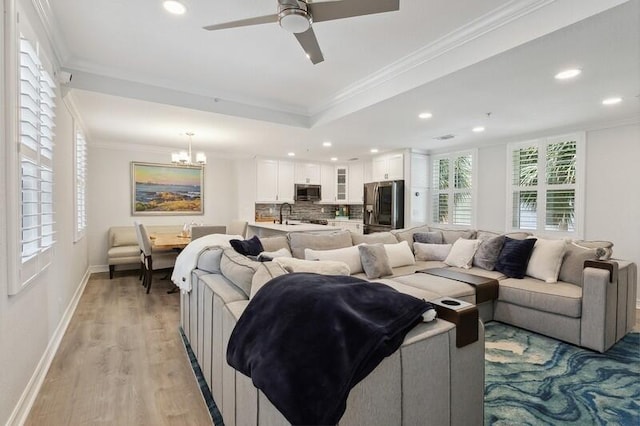 living room with ceiling fan with notable chandelier, light hardwood / wood-style flooring, ornamental molding, and sink