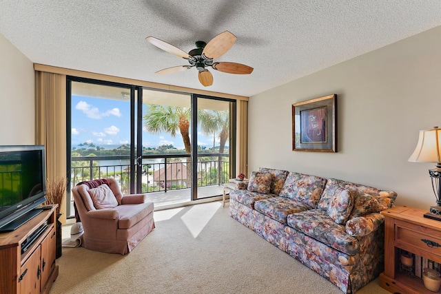 carpeted living room featuring a textured ceiling, ceiling fan, a wall of windows, and a water view