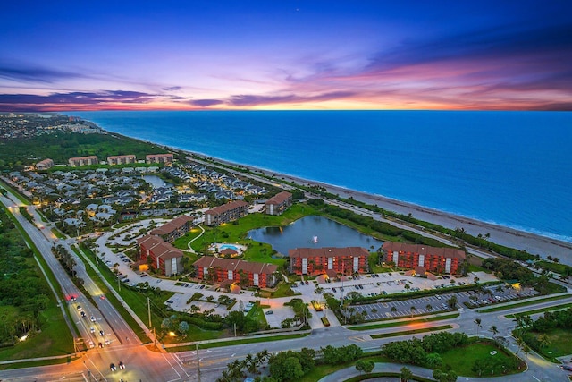 aerial view at dusk featuring a water view and a view of the beach