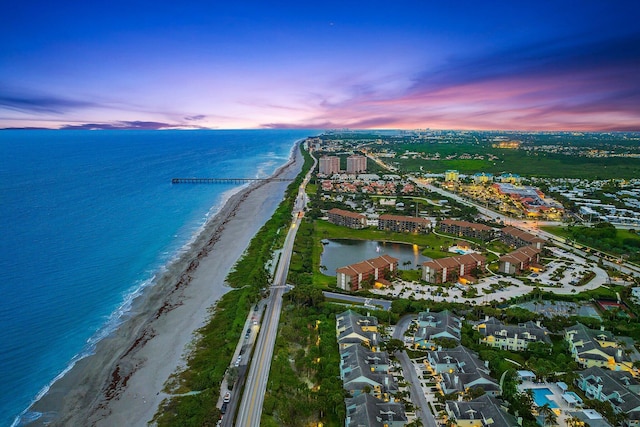 aerial view at dusk featuring a view of the beach and a water view