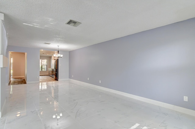 empty room featuring a notable chandelier and a textured ceiling